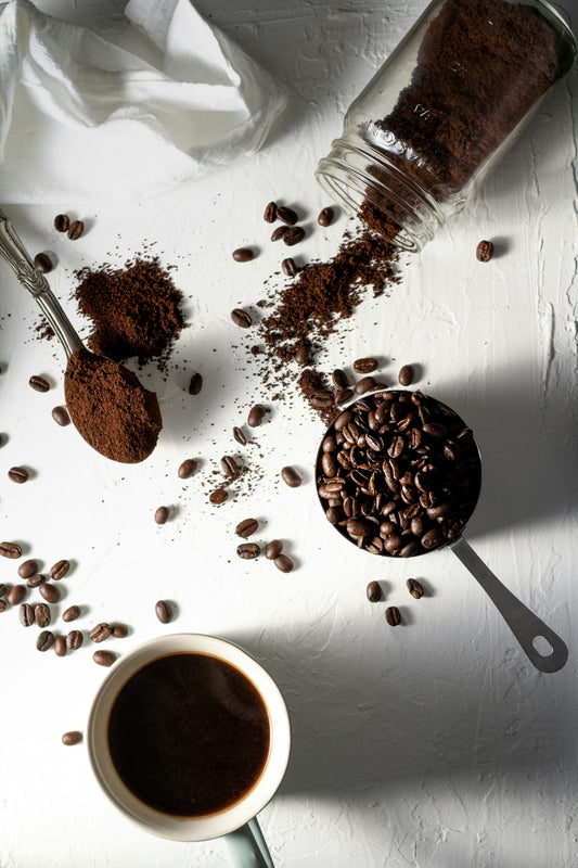 Photo of coffee beans and ground coffee on a white background next to a cup of filter. Taken by Christina Rumf from unsplash. 